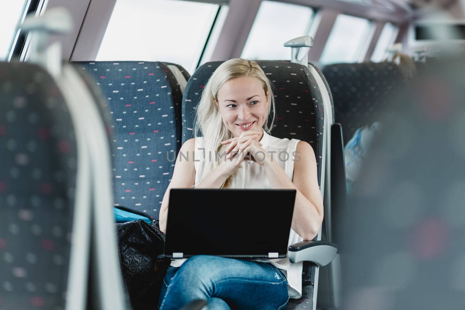 Woman traveling by train smiling and flirting while working on laptop.