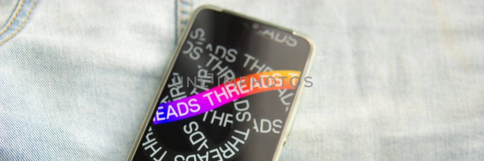 Tver, Russia - July 15, 2023, the threads logo on the smartphone screen lying on the jeans. The threads icon. The logo of the current application. Threads social network. by Annu1tochka