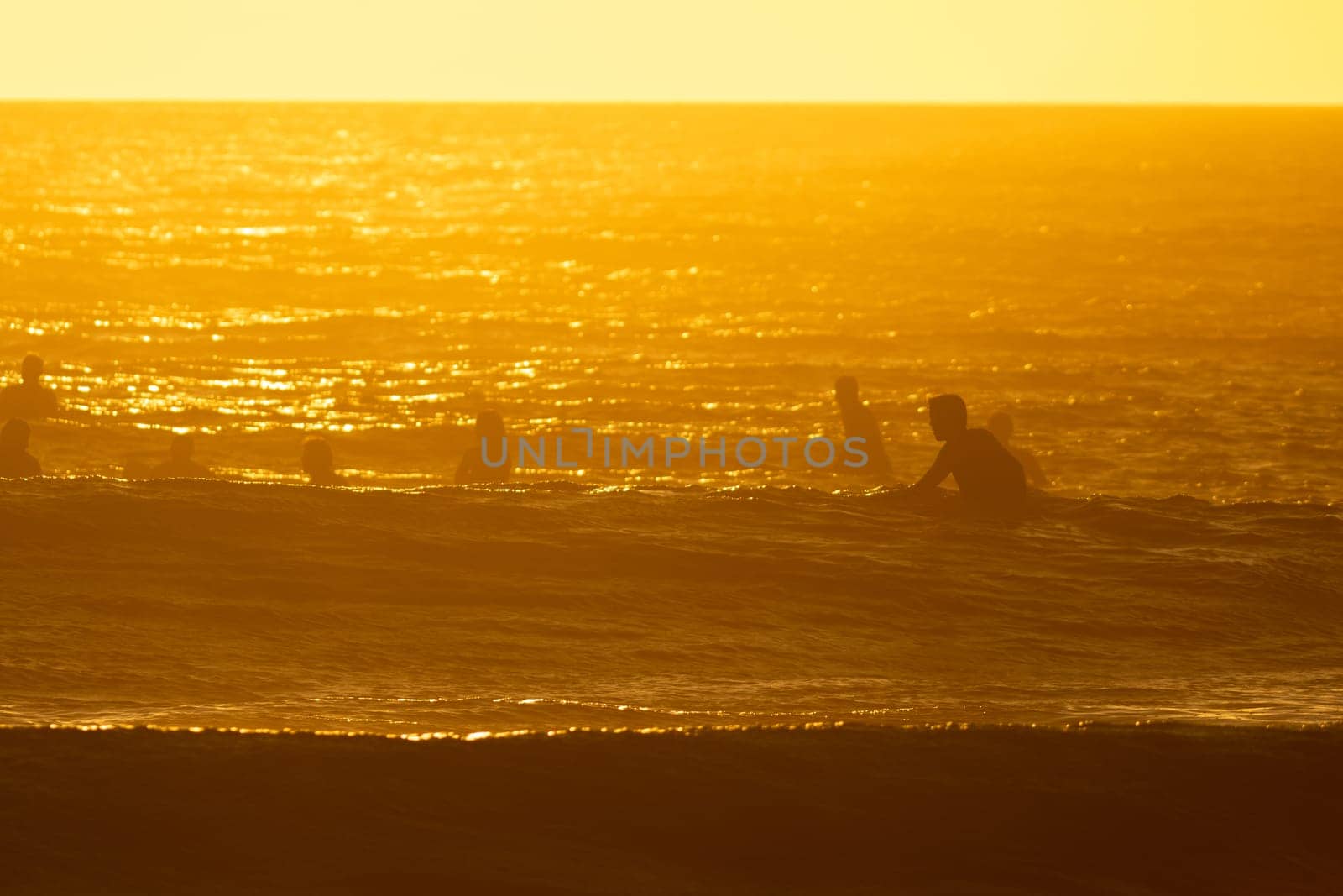 People swimming in the sea at bright orange sunset. Mid shot