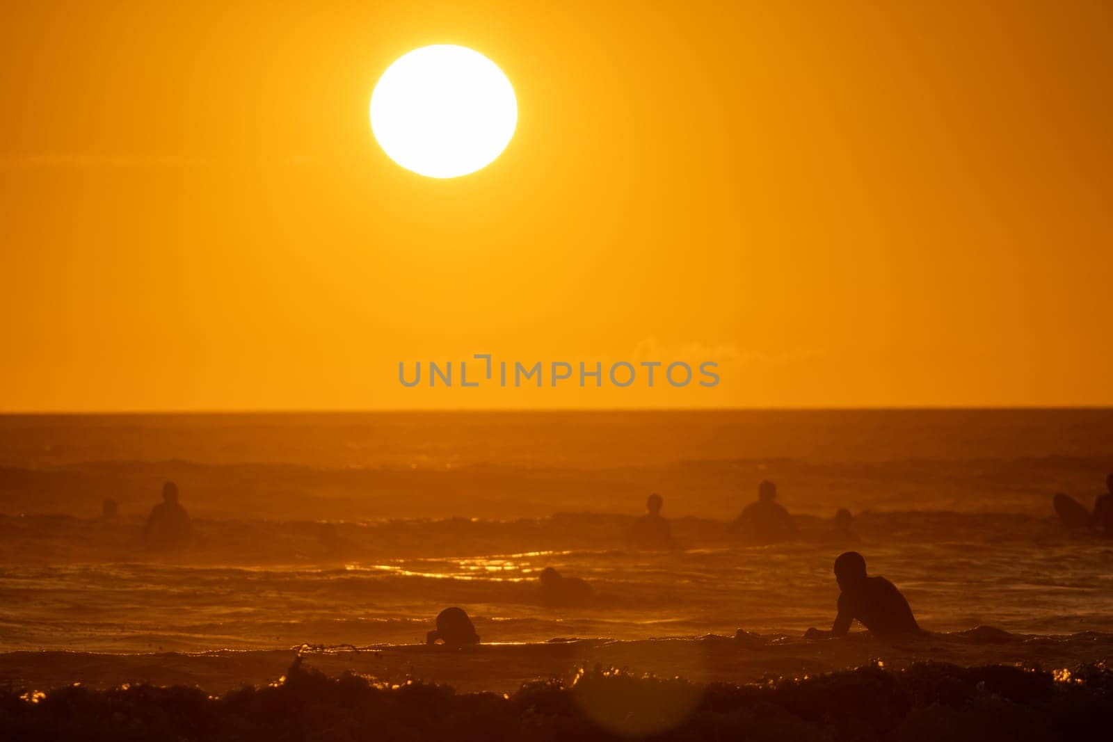 People swimming in the sea at bright orange sunset - huge shining sun. Mid shot