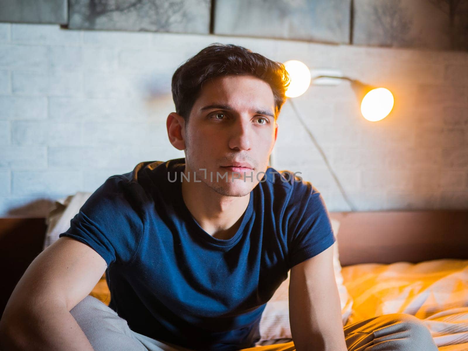 Attractive young man laying on his bed holding remote control, watching TV