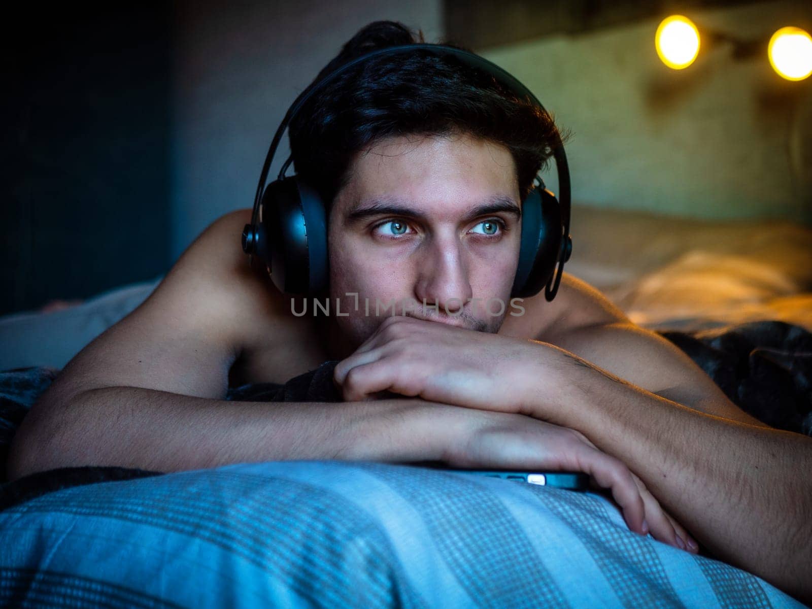 Attractive Young Man Using Headphones Lying Alone On His Bed, Listening to Music and Having a Good Time