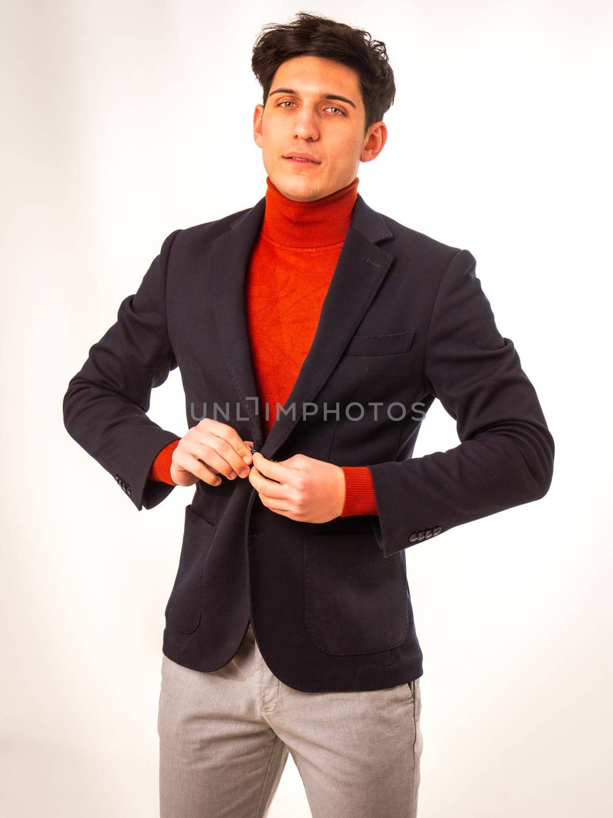 Handsome young male worker in studio shot, standing, looking at camera wearing turtleneck sweater and business suit jacket