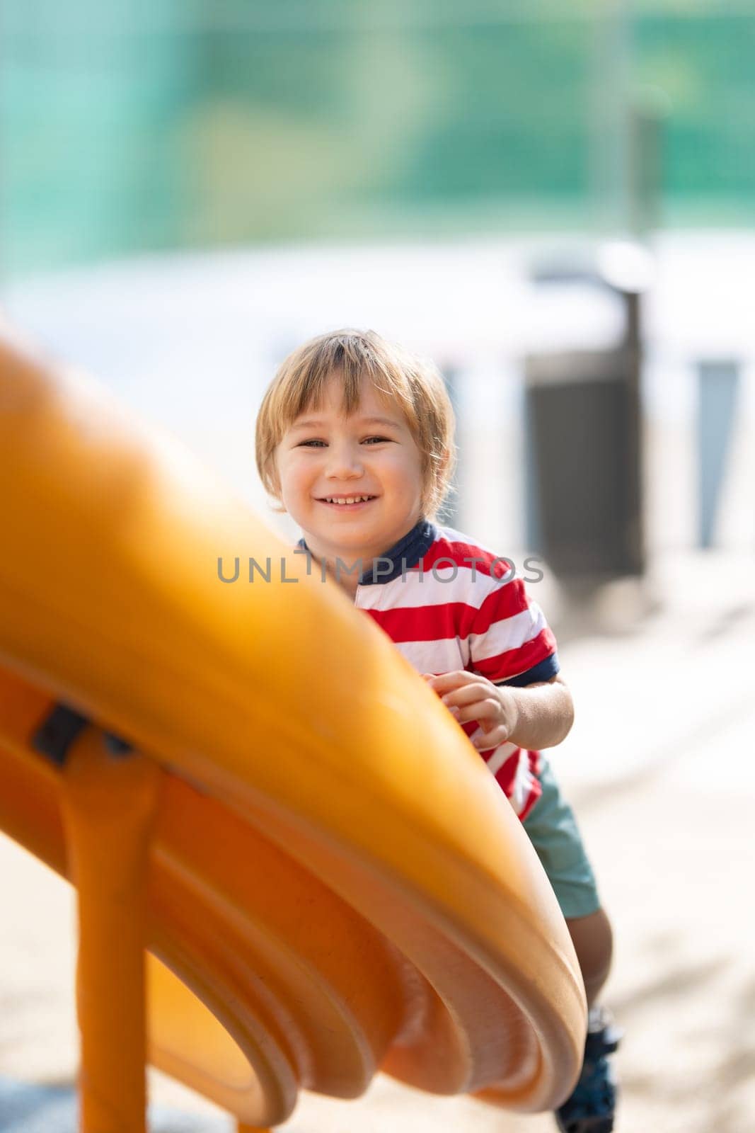 Cute smiling blonde boy climbing up the slide and looking in the camera. Vertical shot