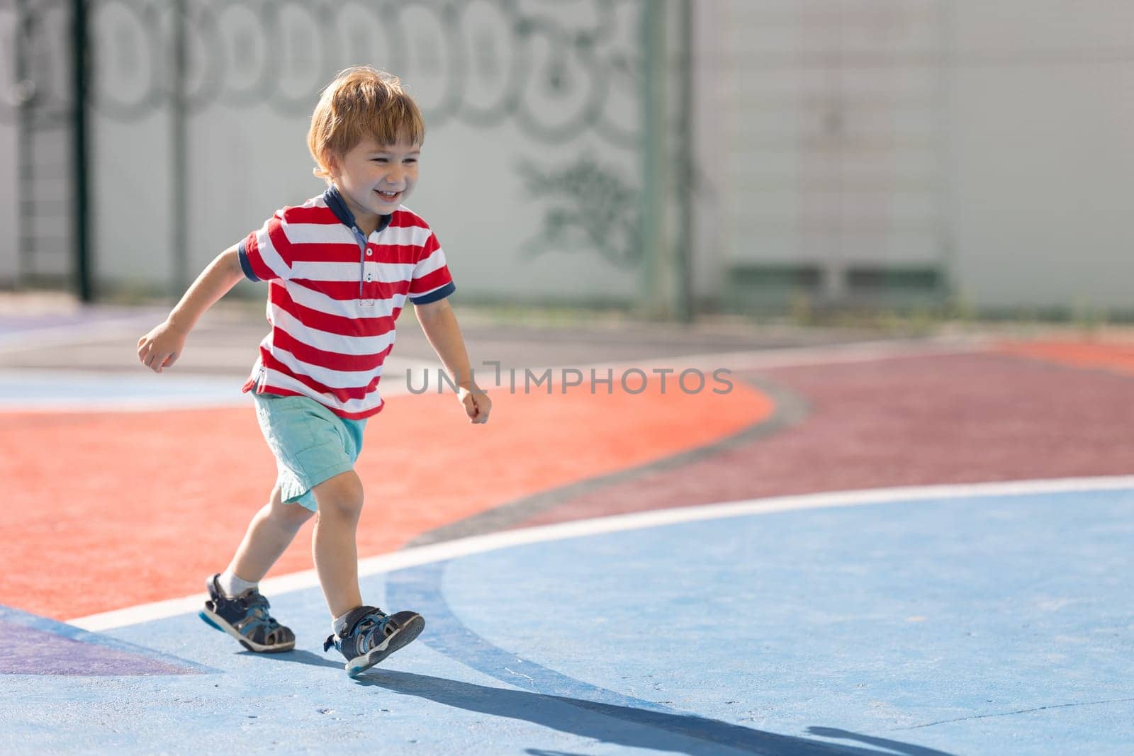 Little blonde smiling boy running on the soccer field. Mid shot