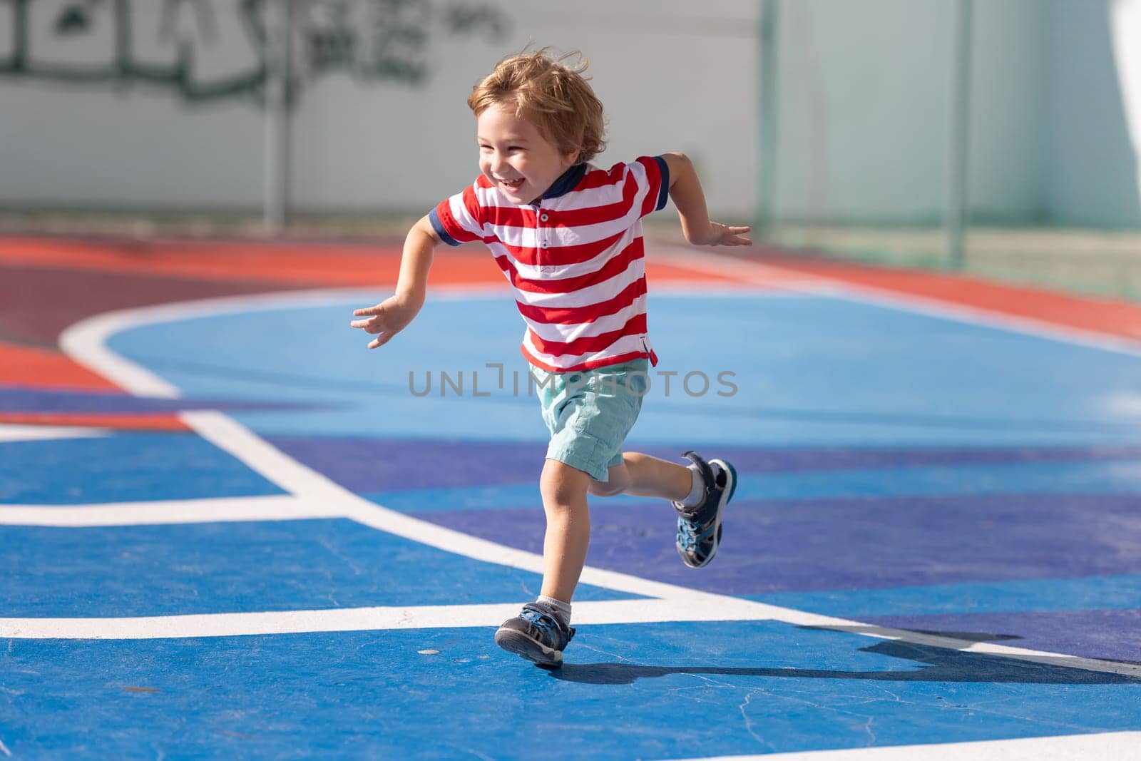 Little blonde smiling boy playing soccer on the playground - running forwards being excited. Mid shot