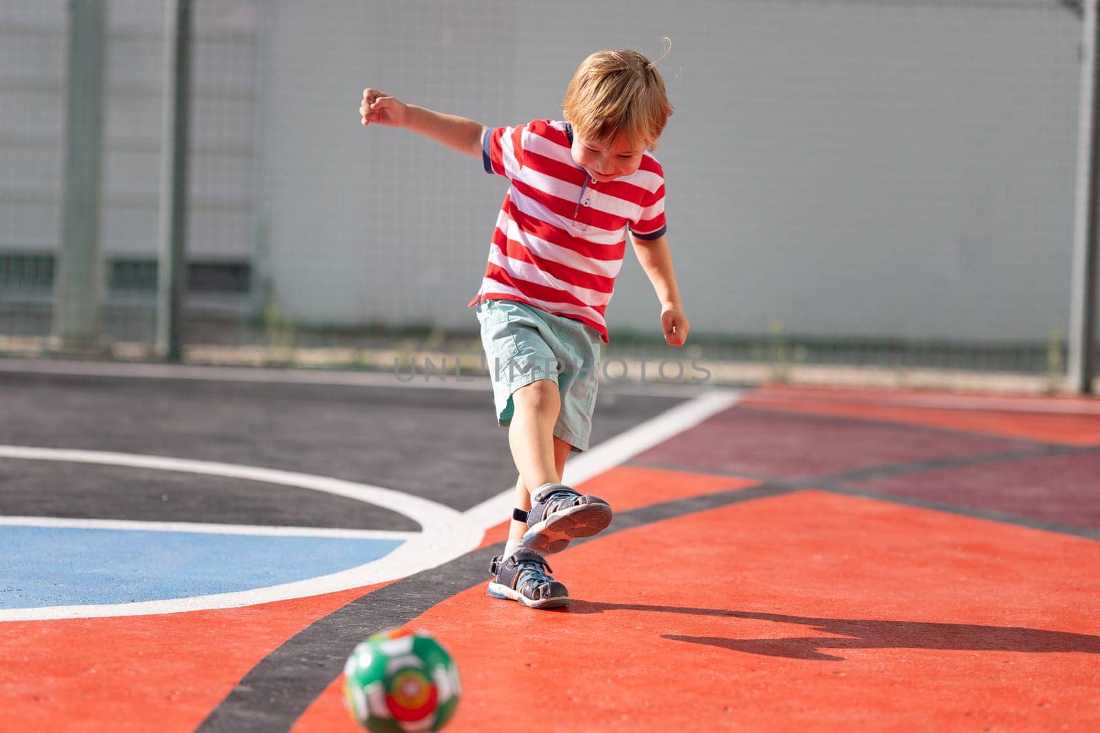 Little blonde smiling boy playing soccer on the playground - hitting back the ball. Mid shot