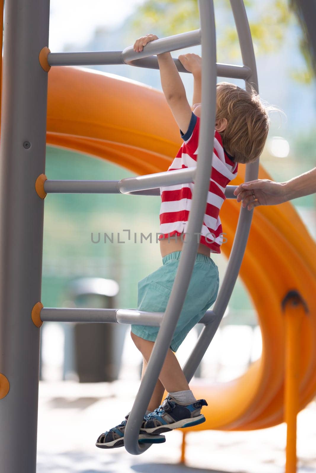 Cute blond boy climbing ladder on playground. Vertical shot