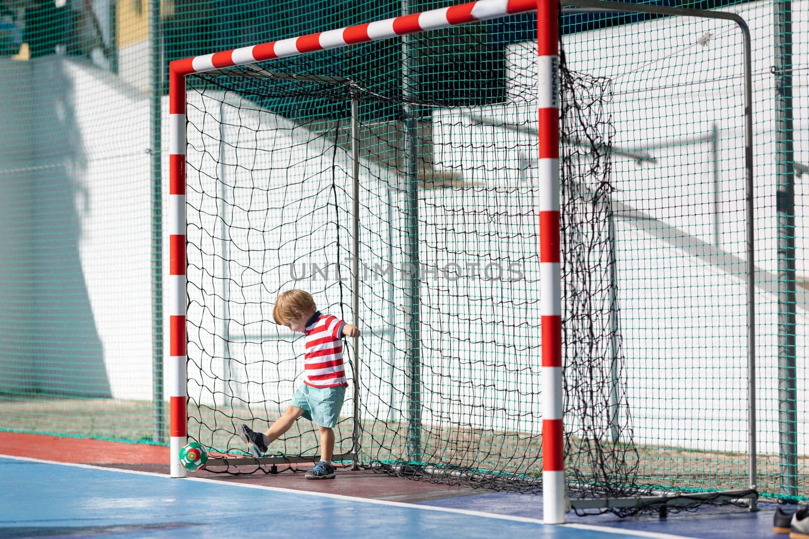 Little blonde smiling boy playing soccer - standing in the gates and hitting back the ball by Studia72
