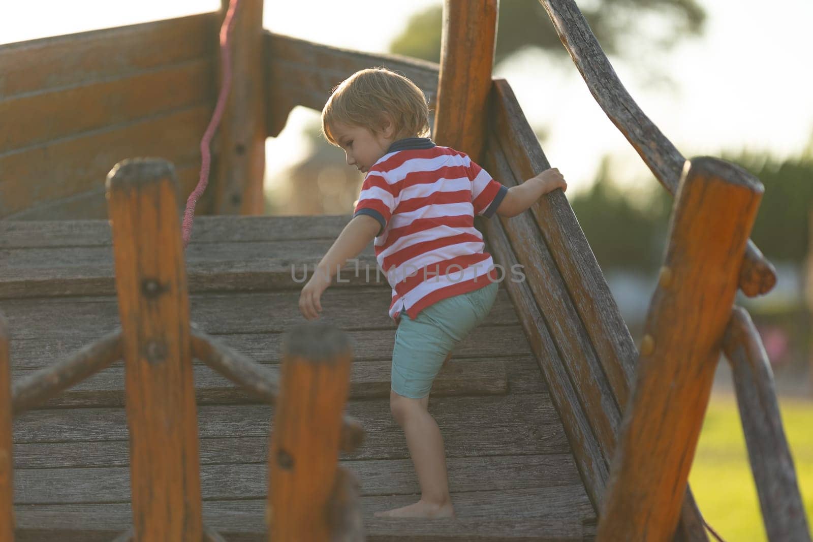 Little cute boy climbing up wooden structure on playground. Mid shot