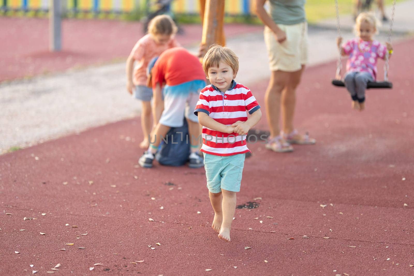 Little cute boy walking on the playground with other kids by Studia72