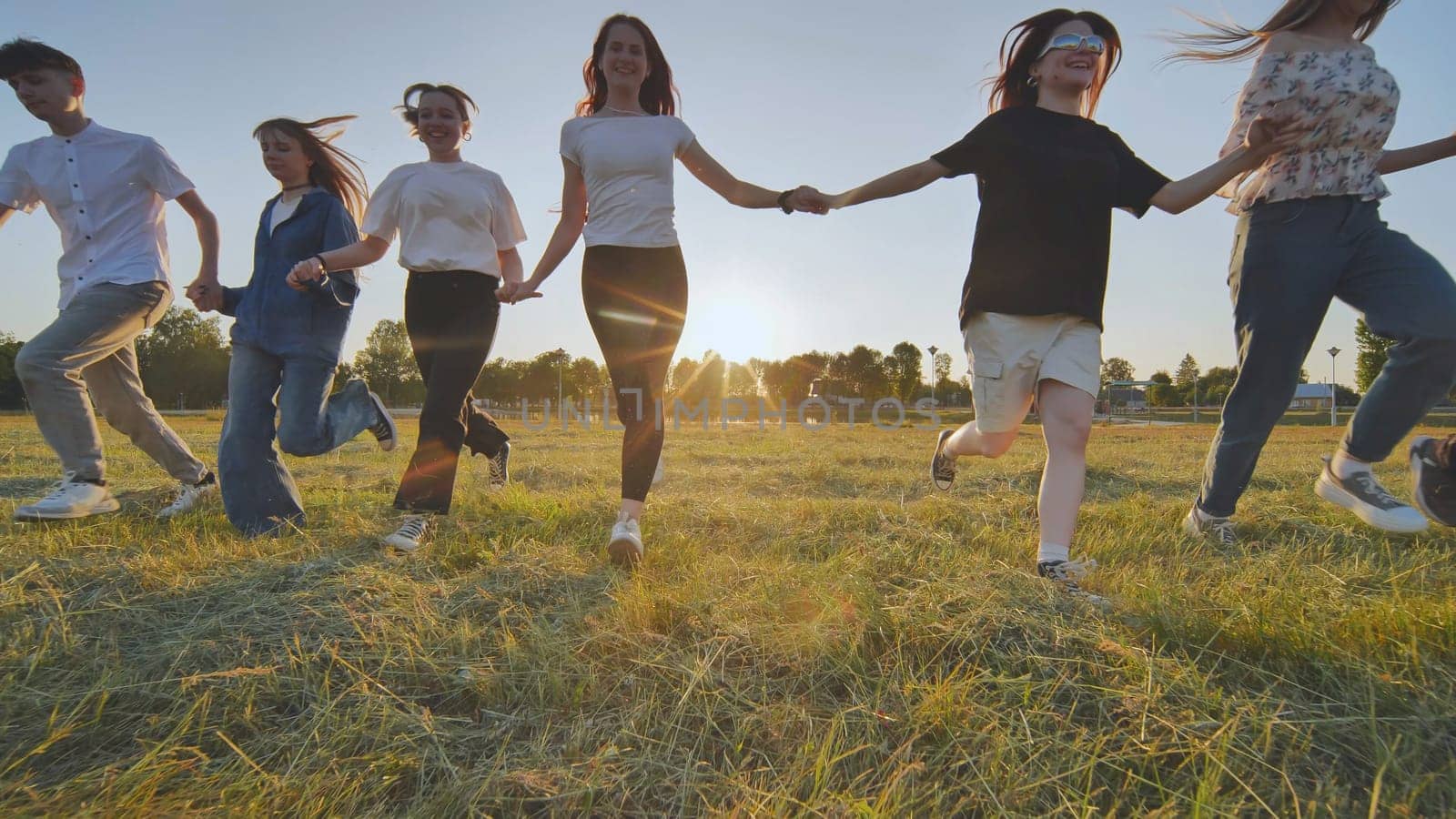 School friends running across the field holding hands at sunset