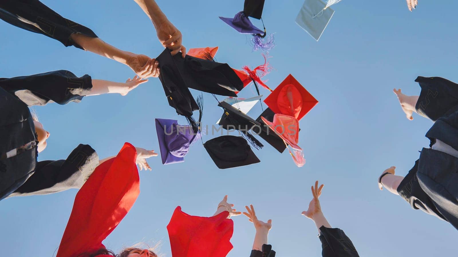 Graduates tossing multicolored hats against a blue sky. by DovidPro