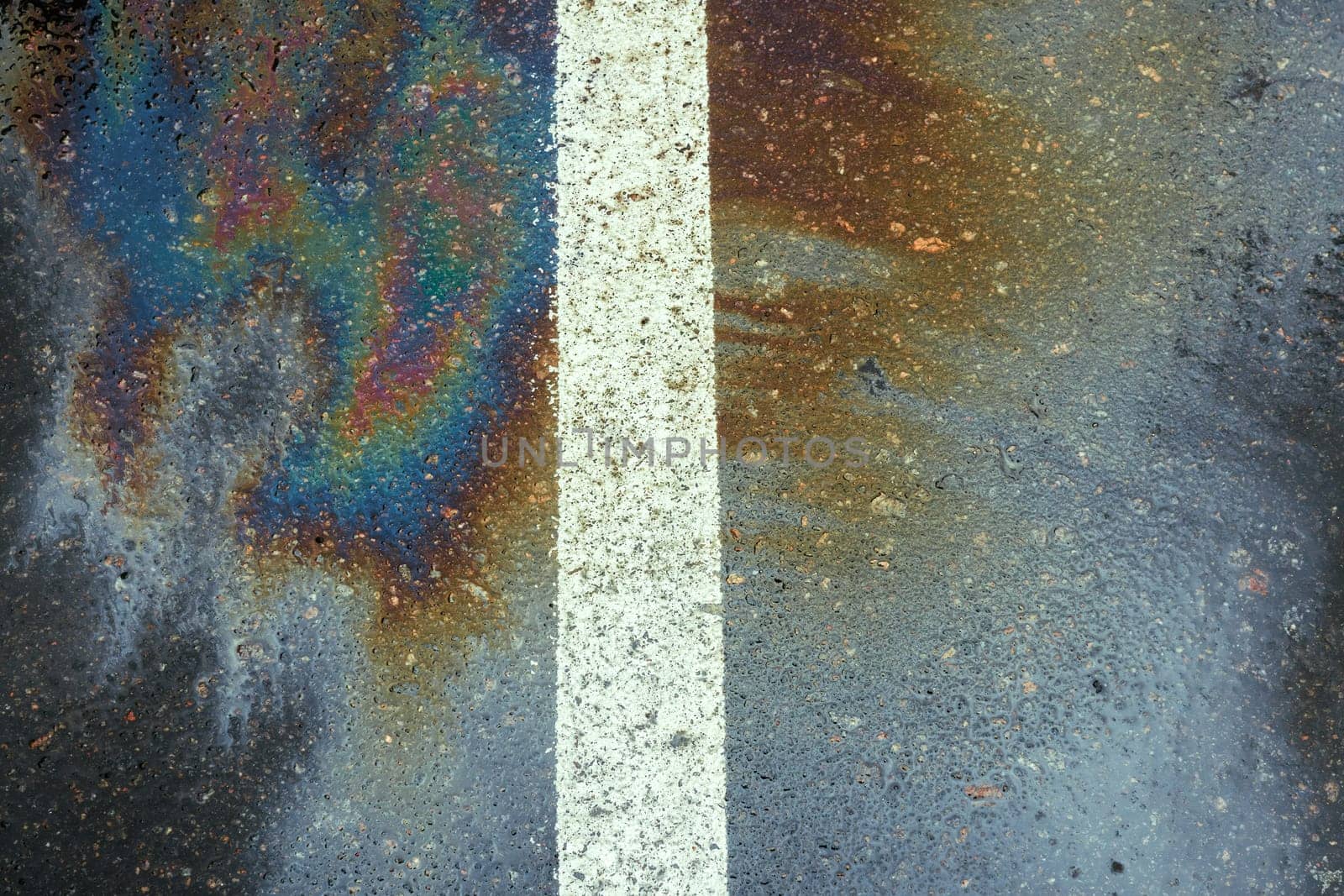 Oil spill on dark wet asphalt, parking lot with dividing lines.