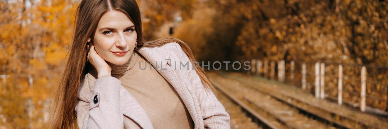 A beautiful long-haired woman walks through the autumn streets. Railway, autumn leaves, a woman in a light coat.