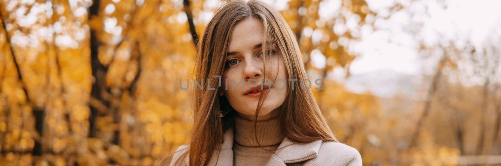 A beautiful long-haired woman walks through the autumn streets. Railway, autumn leaves, a woman in a light coat.