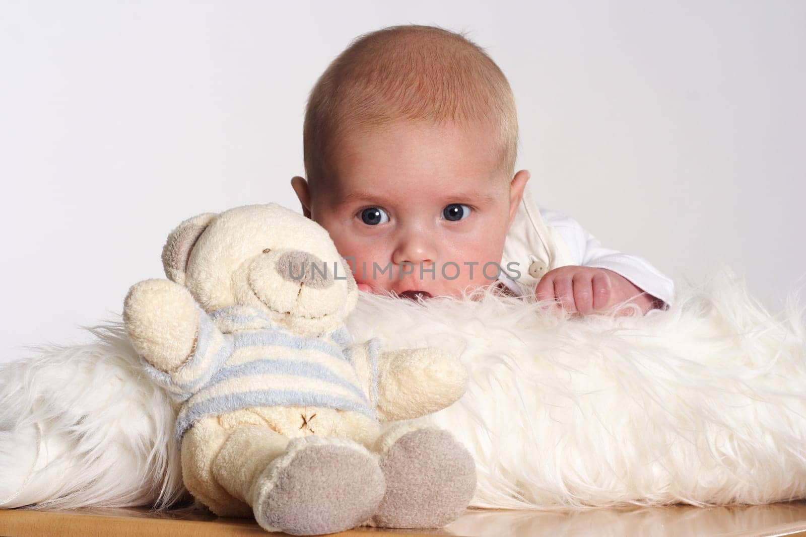 Small child lying on a white fur with a teddy bear