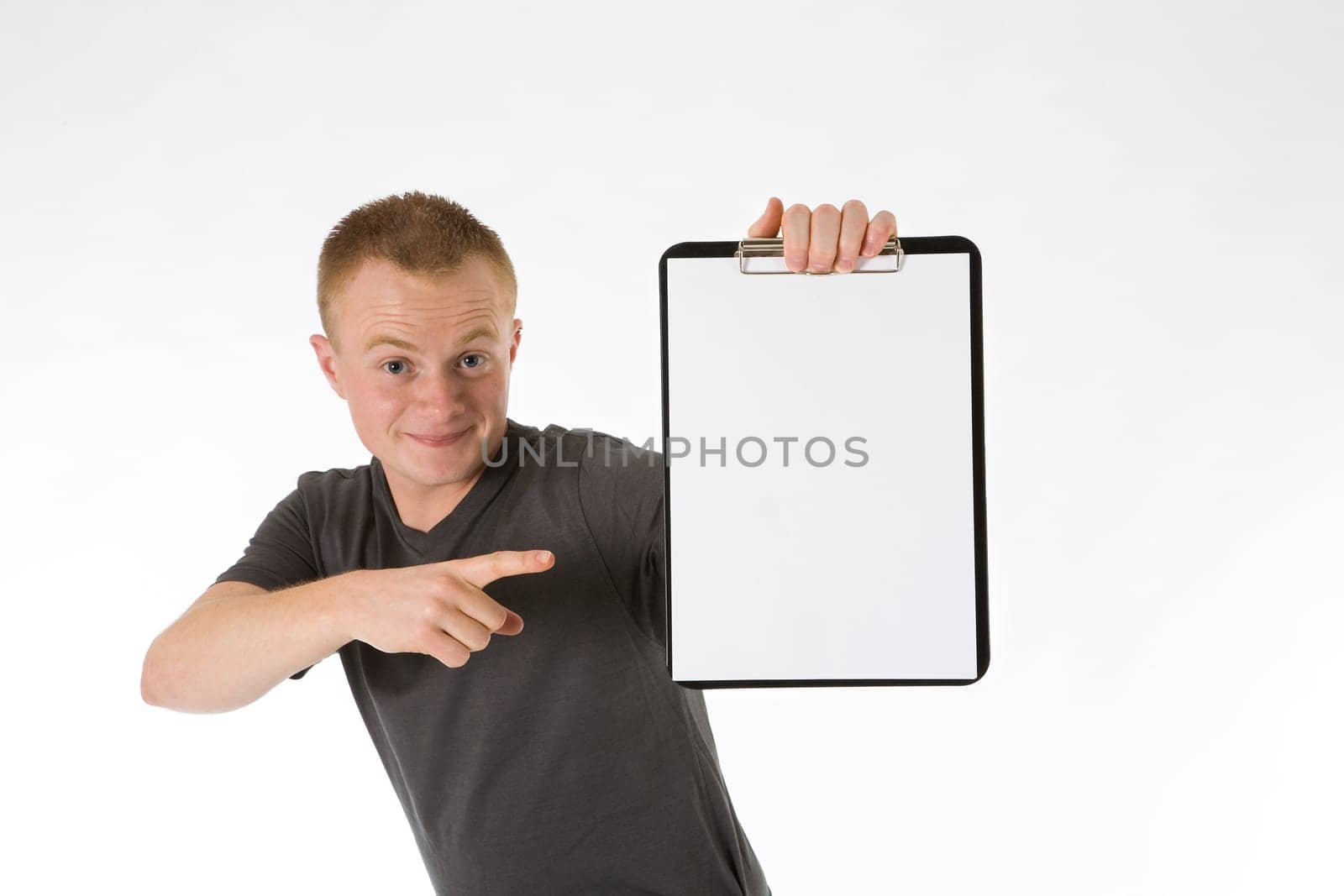 A young man holds a paper clipboard (white sheet for his own text),points to it and makes a funny face.