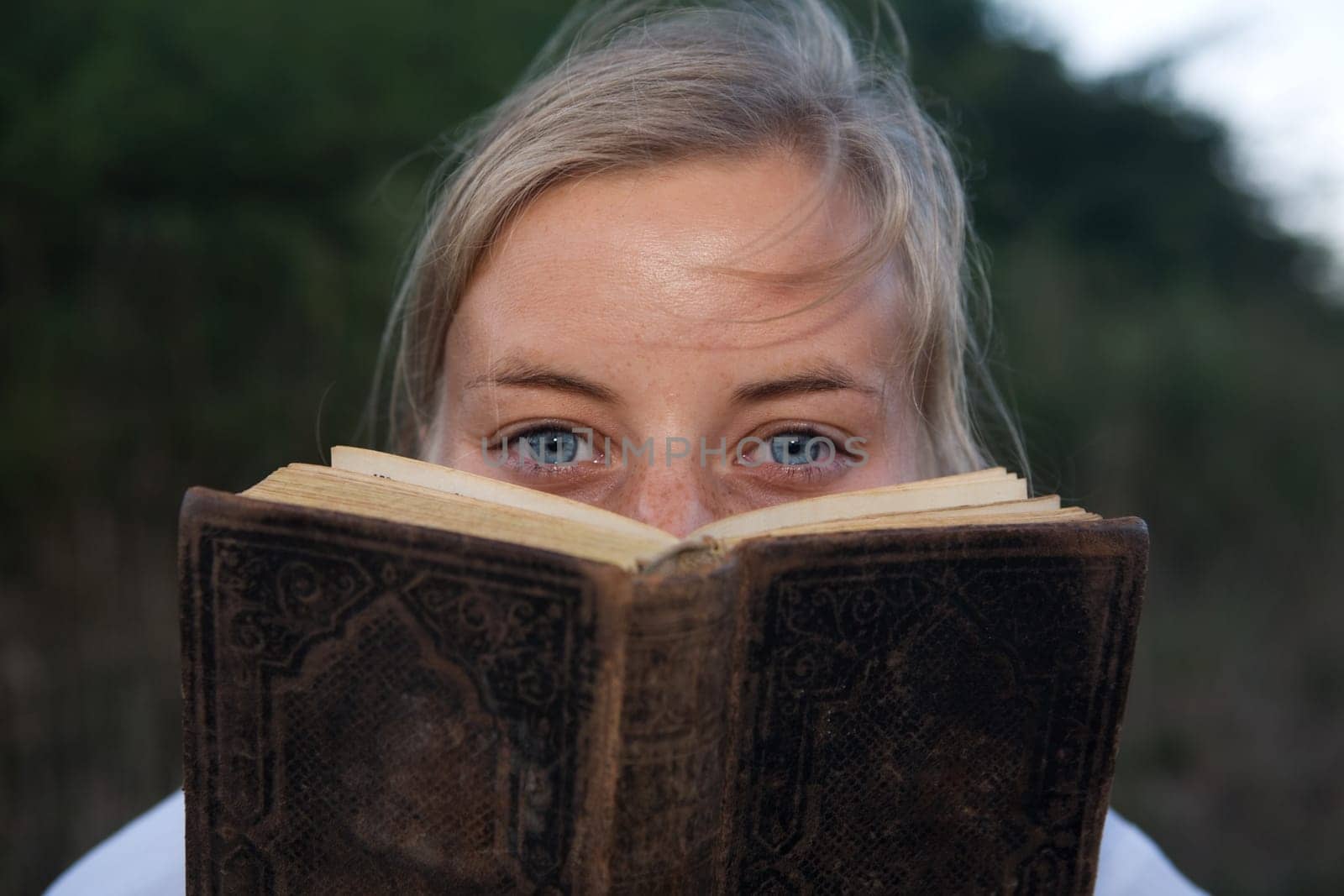 A young woman peeks out from behind an old book
