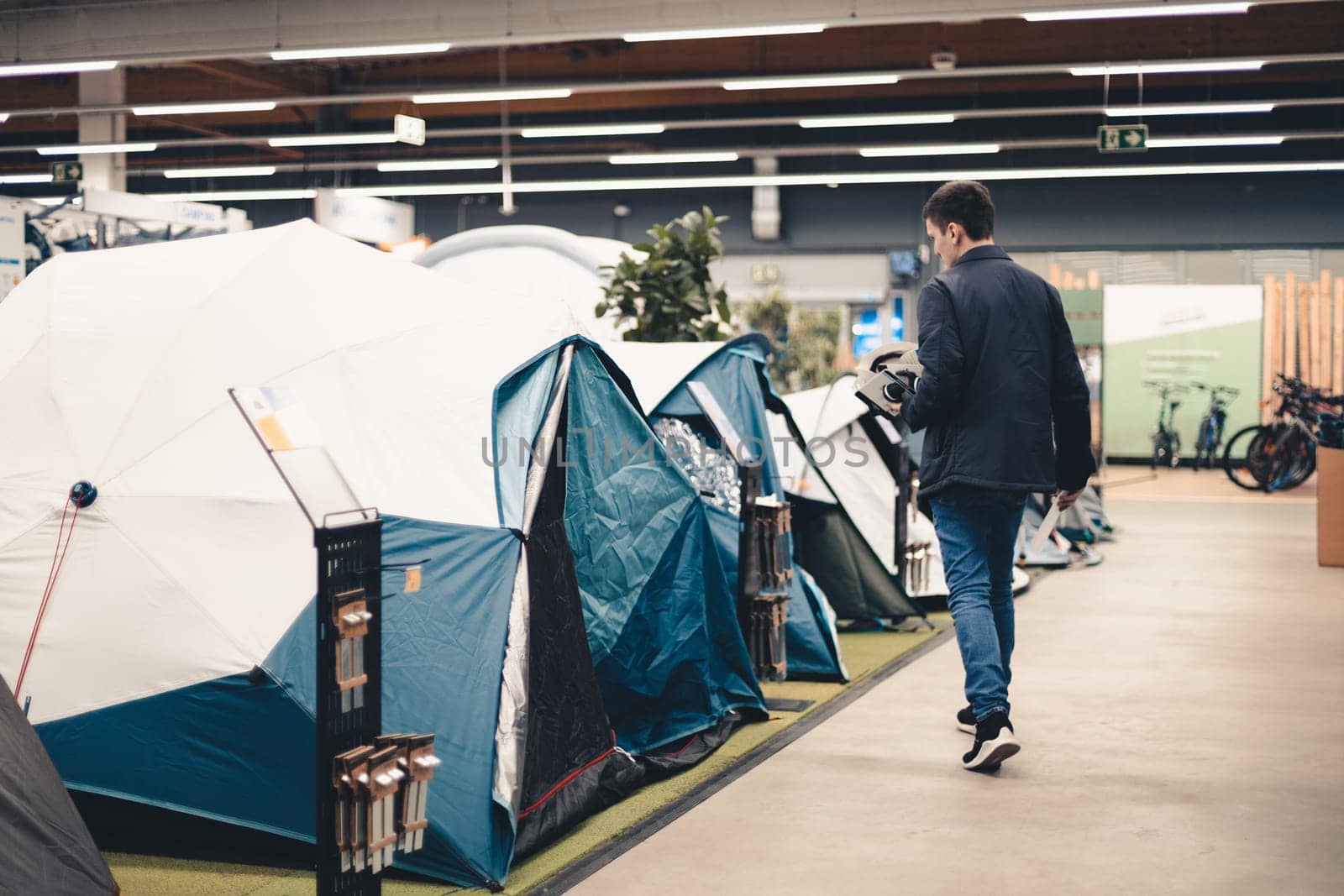 A young man examines the tents in the store. by Nataliya