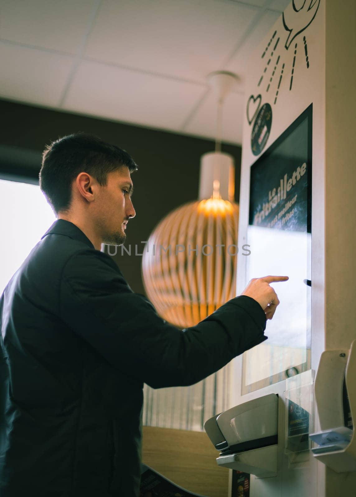 A young man makes an order for fast food on a scoreboard screen in a diner. by Nataliya