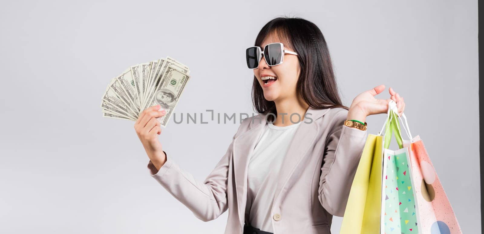 Woman with glasses confident shopper smile holding online shopping bags multicolor and dollar money banknotes on hand by Sorapop