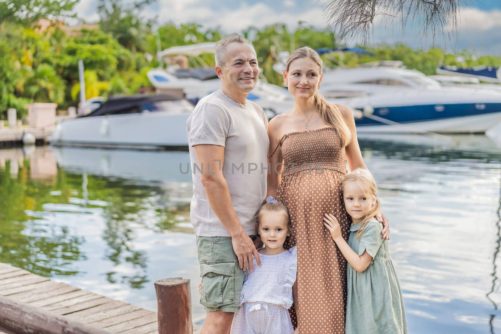A happy, mature couple over 40 with their two daughters enjoying a leisurely walk on the waterfront, their joy evident as they embrace the journey of pregnancy later in life by galitskaya