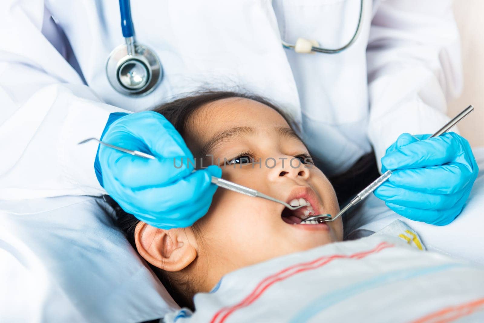 Doctor examines oral cavity of little child uses mouth mirror to checking teeth cavity by Sorapop