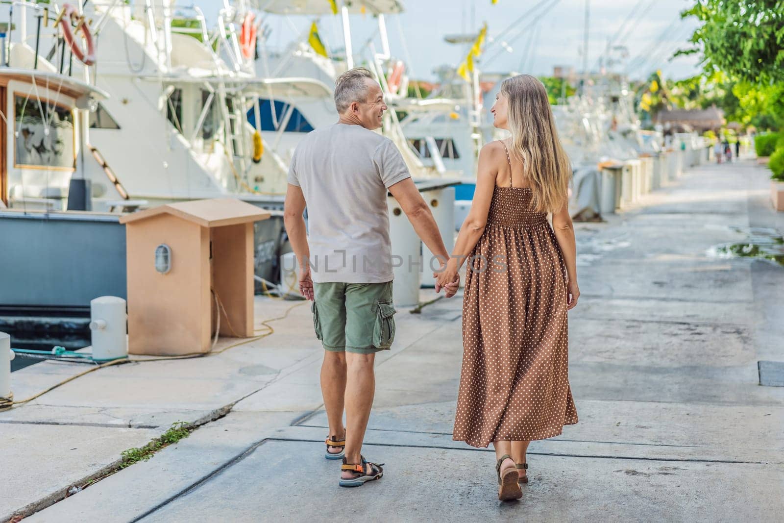 A happy, mature couple over 40, enjoying a leisurely walk on the waterfront, their joy evident as they embrace the journey of pregnancy later in life by galitskaya