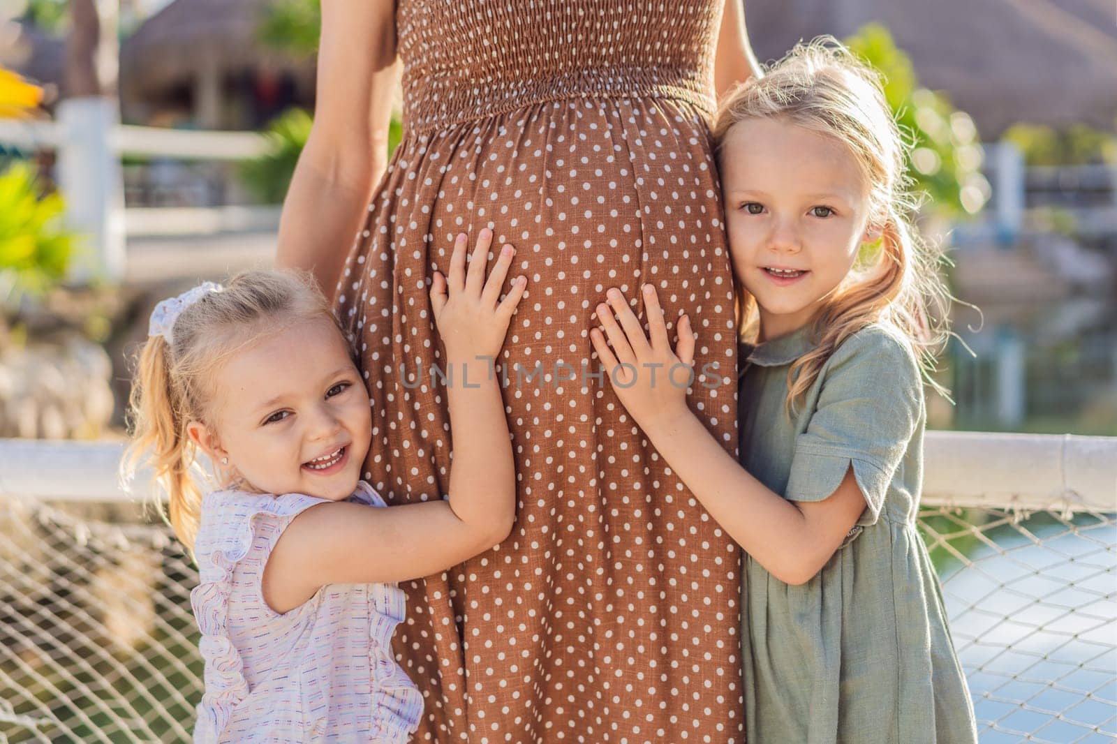 Sisters' love blooms as they tenderly embrace their mother's pregnant belly, sharing anticipation and affection for their soon-to-arrive sibling by galitskaya