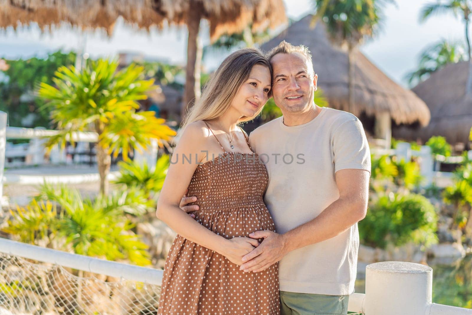 A happy, mature couple over 40, enjoying a leisurely walk in a park, their joy evident as they embrace the journey of pregnancy later in life by galitskaya