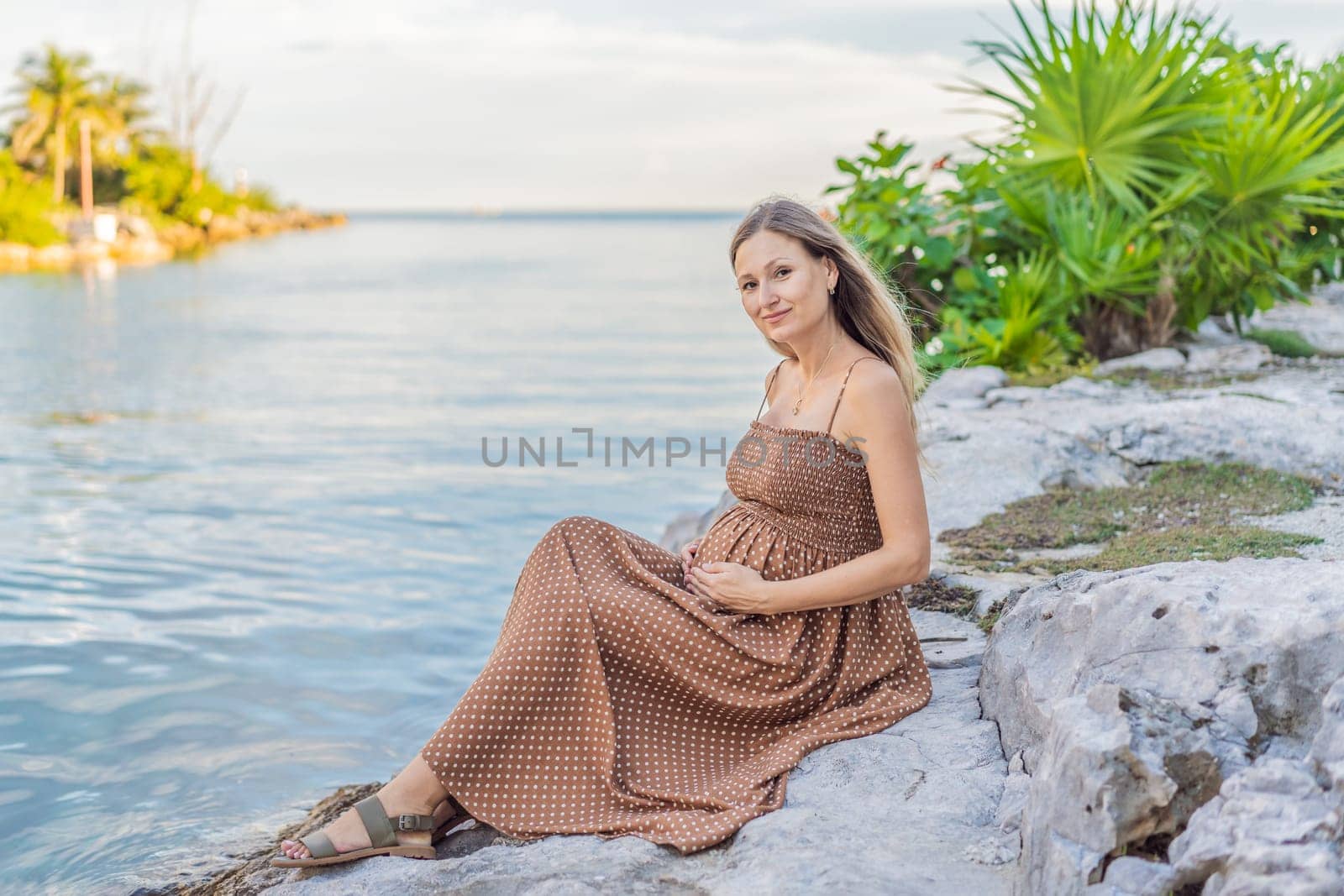 Pregnant woman hugging her tummy standing outdoors surrounded by nature. Pregnancy, expectation, motherhood concept.