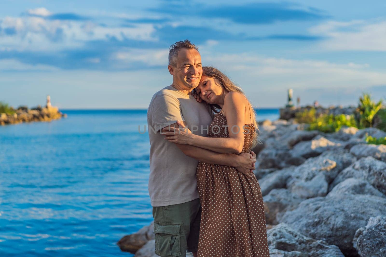 A happy, mature couple over 40, enjoying a leisurely walk on the waterfront On the Sunset, their joy evident as they embrace the journey of pregnancy later in life.