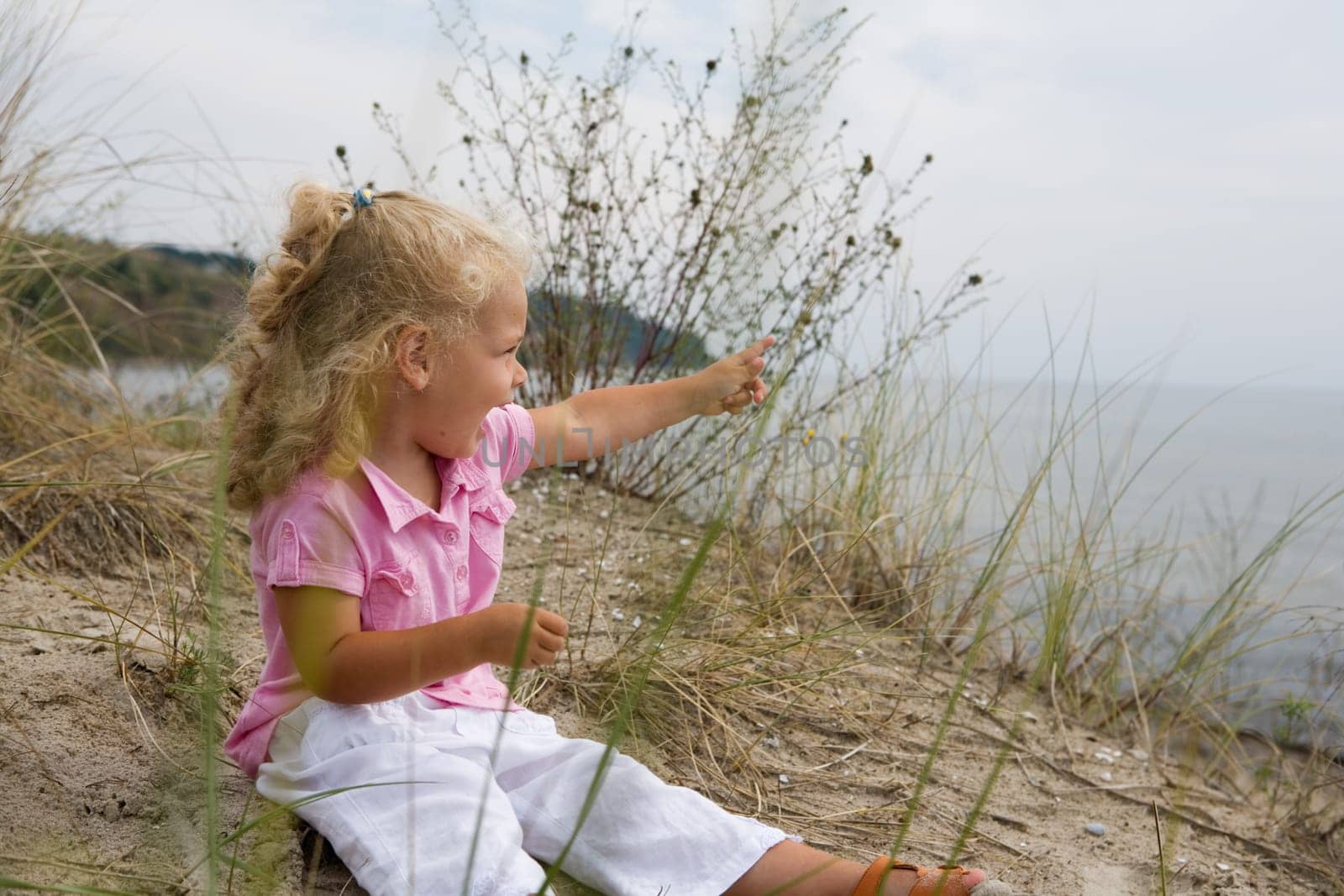 A little girl sits on the beach and points her finger at something