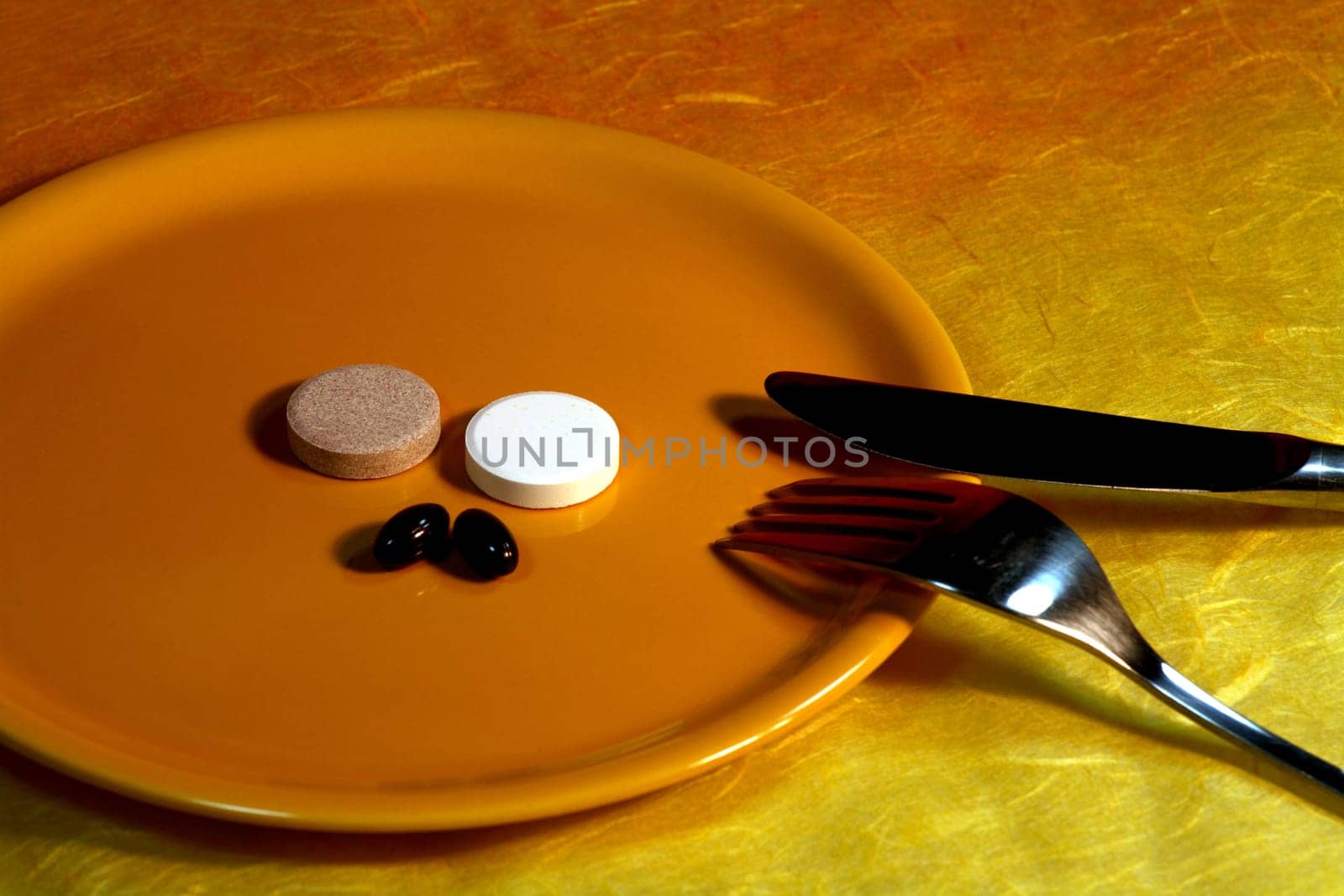 Vitamin tablets on a yellow plate with a knife and fork