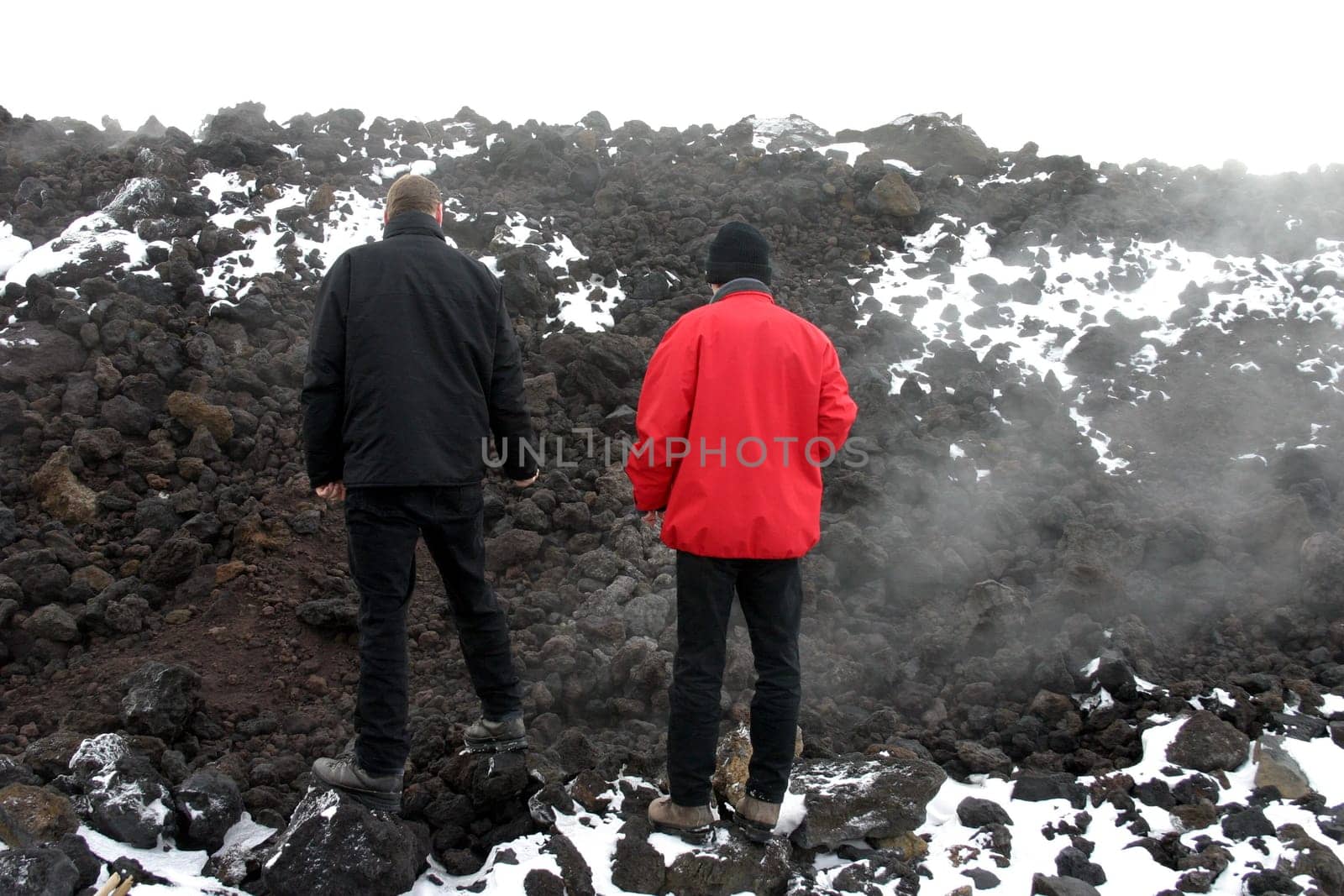 Two men on a steaming lava field of Mount Etna in Sicily