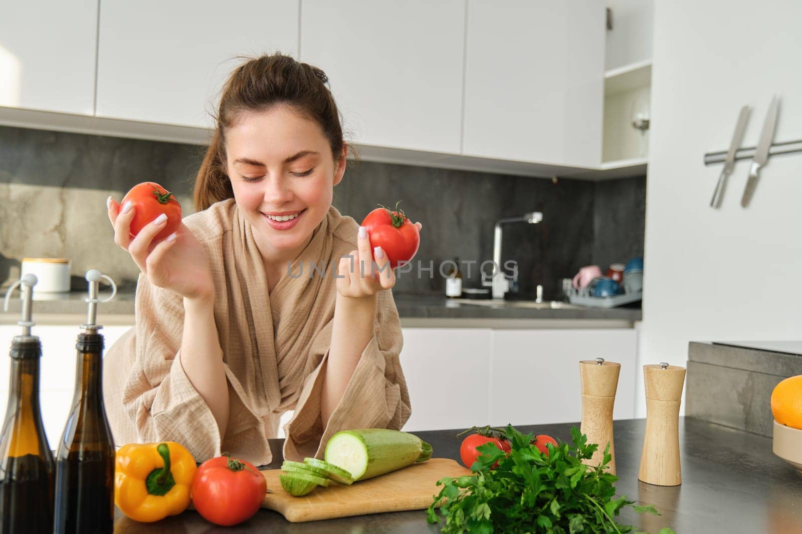 Portrait of beautiful woman cooking in the kitchen, chopping vegetables on board, holding tomatoes, lead healthy lifestyle with preparing fresh salads, vegan meals by Benzoix