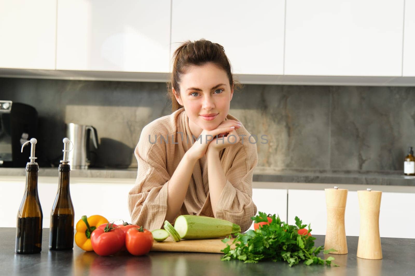 Healthy lifestyle. Young woman in bathrobe preparing food, chopping vegetables, cooking dinner on kitchen counter, standing over white background.