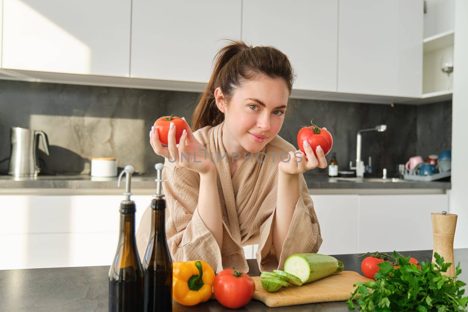 Portrait of woman cooking at home in the kitchen, holding tomatoes, preparing delicious fresh meal with vegetables, standing near chopping board.