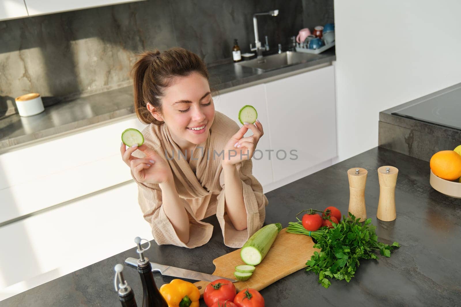 Portrait of beautiful brunette woman in the kitchen, wearing bathrobe, chopping vegetables on board, cooking healthy vegetarian food, preparing salad, making a meal by Benzoix