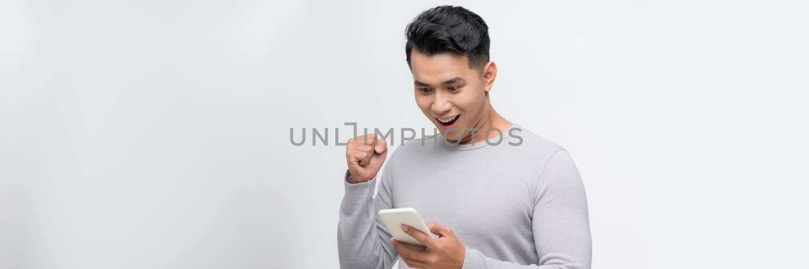 A happy young man holding mobile phone and celebrating success isolated over white background by makidotvn