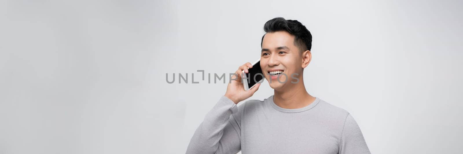 Handsome young man talking on smartphone against grey background.