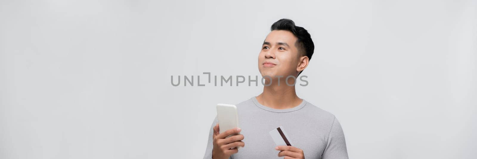 Young asian smiling attractive man hold mobile cell phone credit bank card shopping online. Panorama