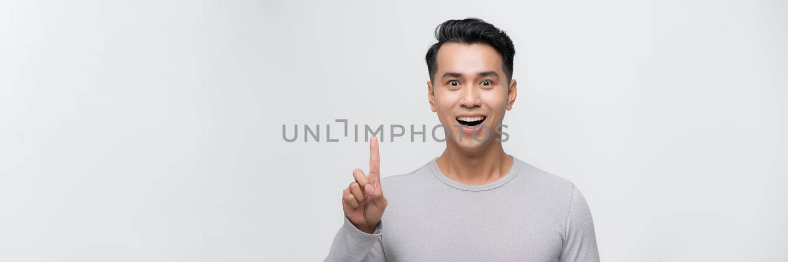 Attractive young man pointing up with his finger isolated on gray background