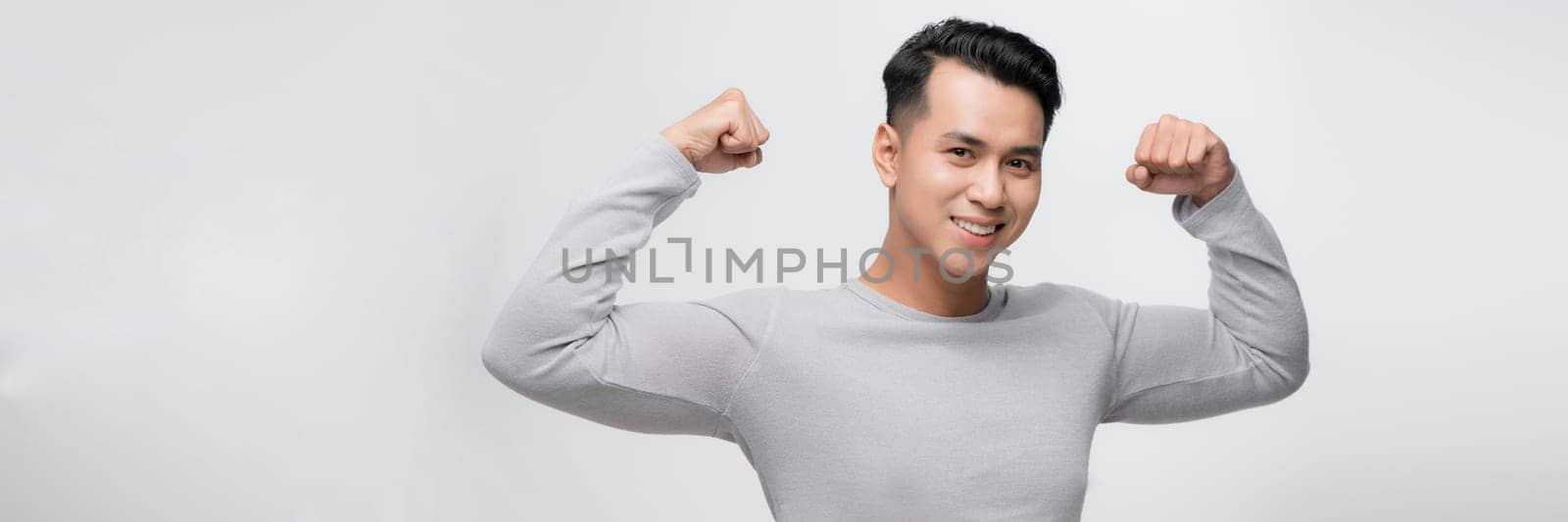 Young handsome asian man over white backgroundshowing arms muscles smiling proud.