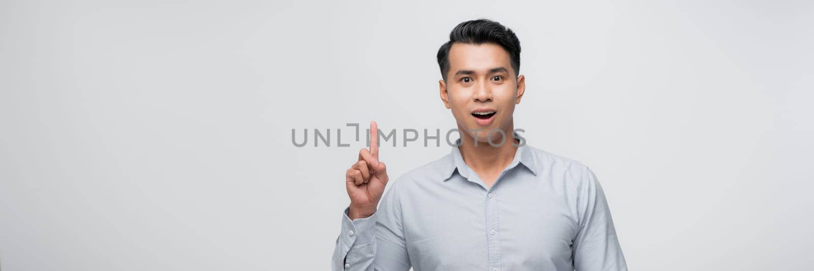 Attractive young man pointing up with his finger isolated on gray background