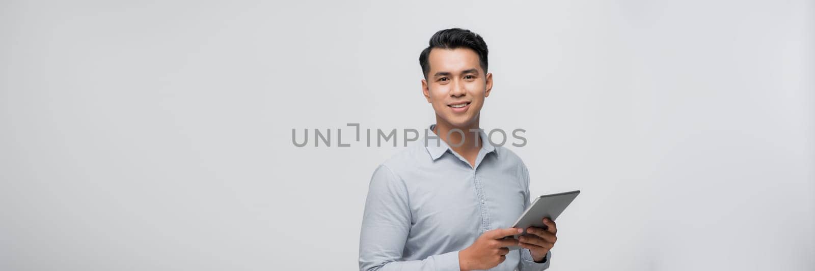 A portrait of a young asian man holding a digital touch screen tablet computer on white background. by makidotvn