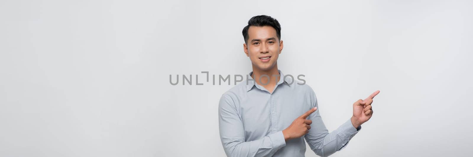 Young handsome man with a big smile on face, pointing with hand and finger to the side looking at the camera.