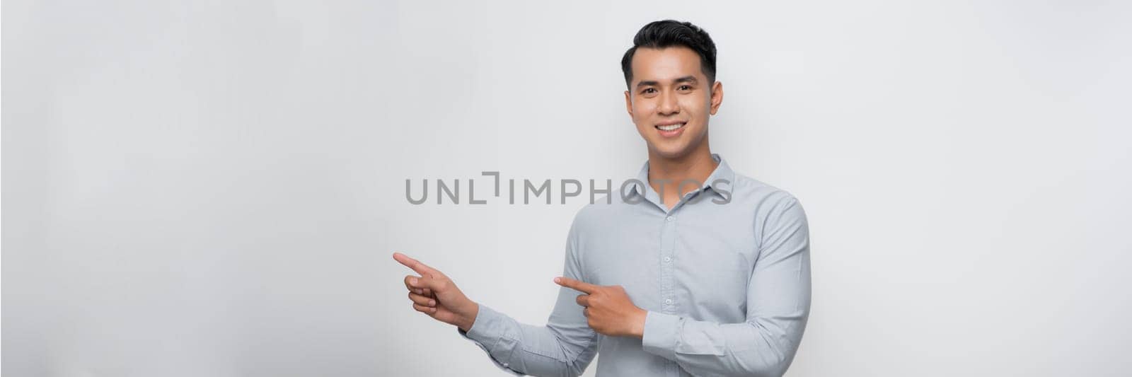 smiling young handsome Asian man pointing fingers in empty space aside