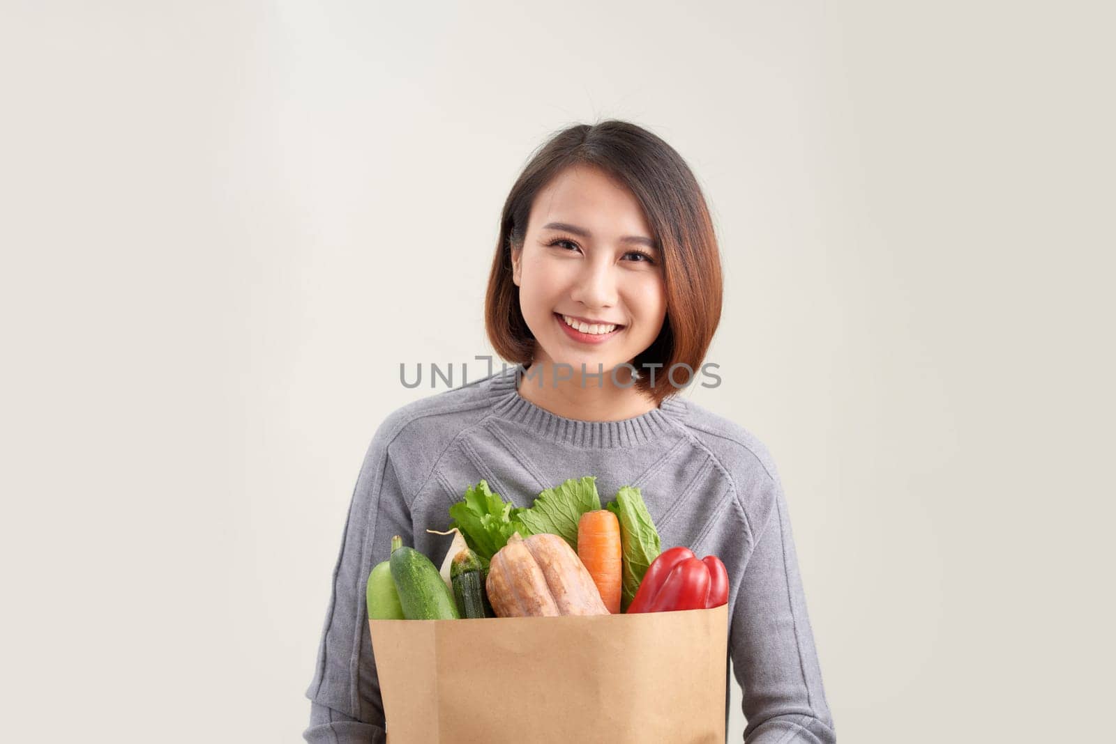Young asian woman smiles embraces paper bag with fresh products returns from supermarket  by makidotvn